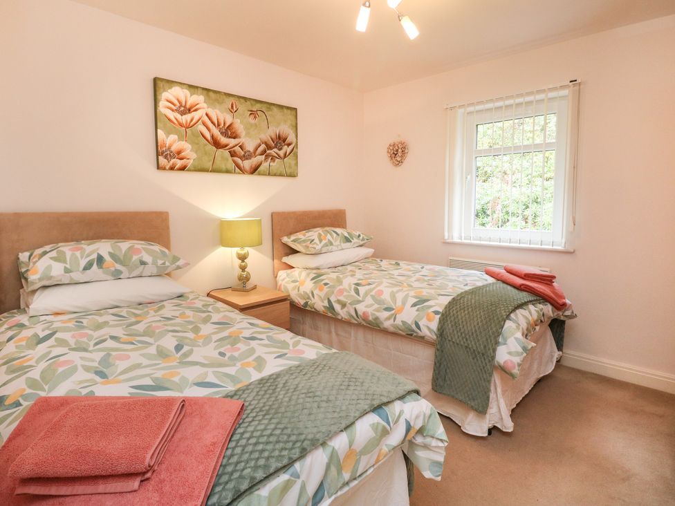 A bedroom with two single beds bedside table lamp window and floral painting at 4 River Court in Invergarry