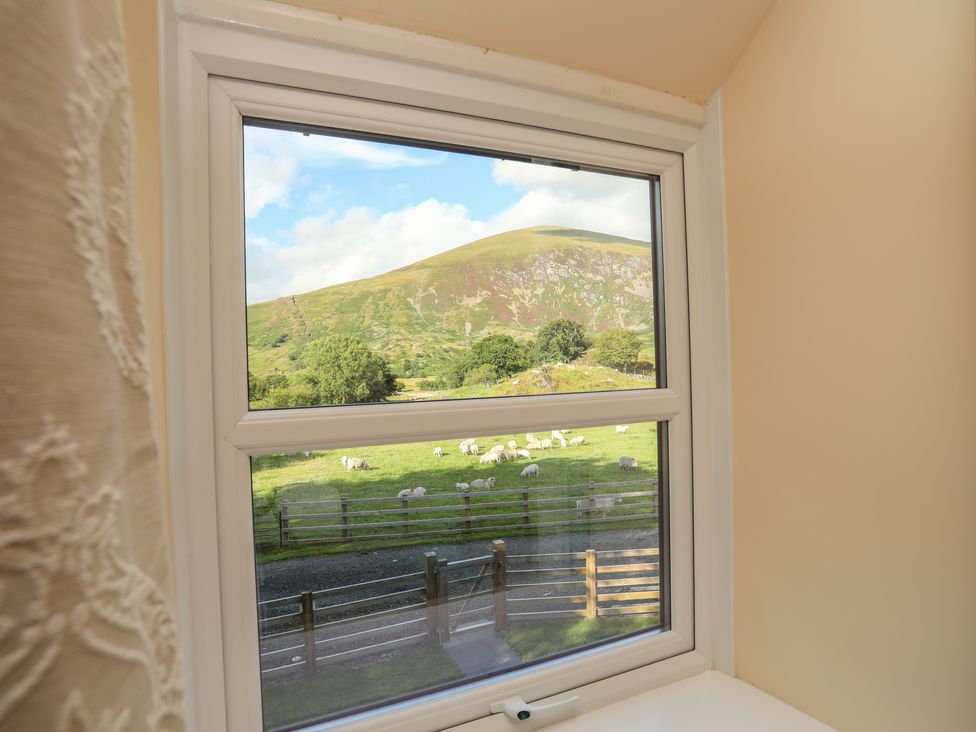 A window view of a fenced green field with sheep and a hill in the background at Ty Coch Betws Garmon near Caernarfon