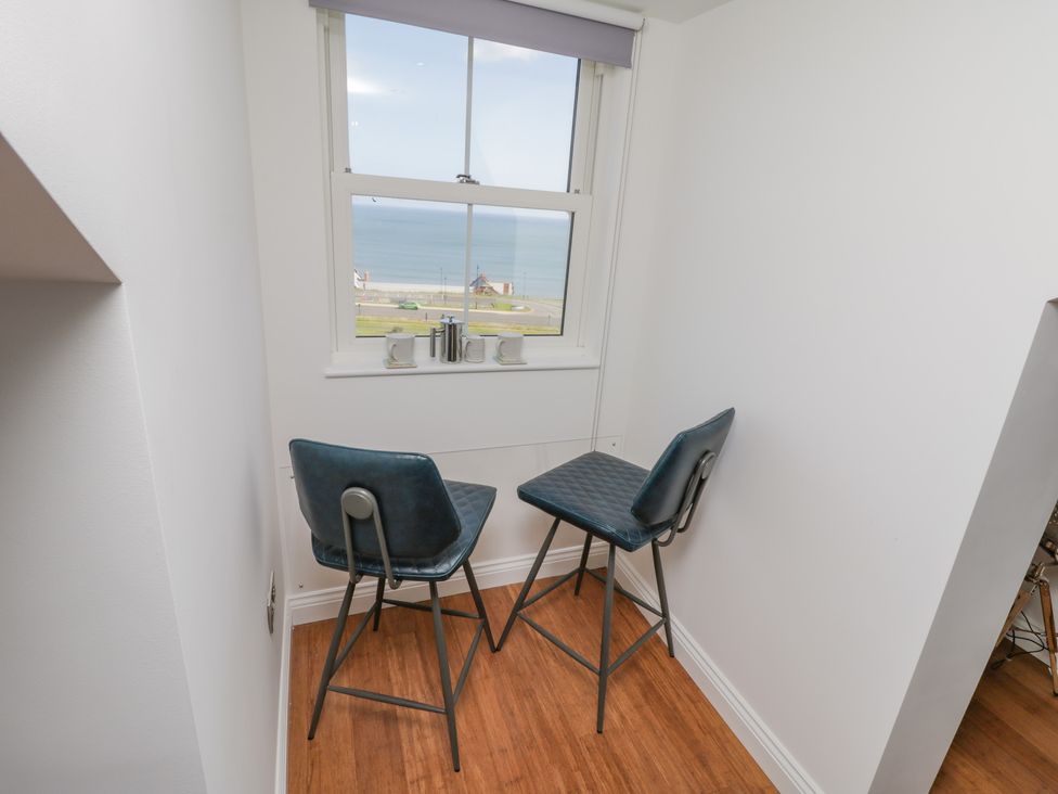 A small dining area with two blue chairs and a glass table by a window overlooking the sea at Foxton Penthouse in Whitby