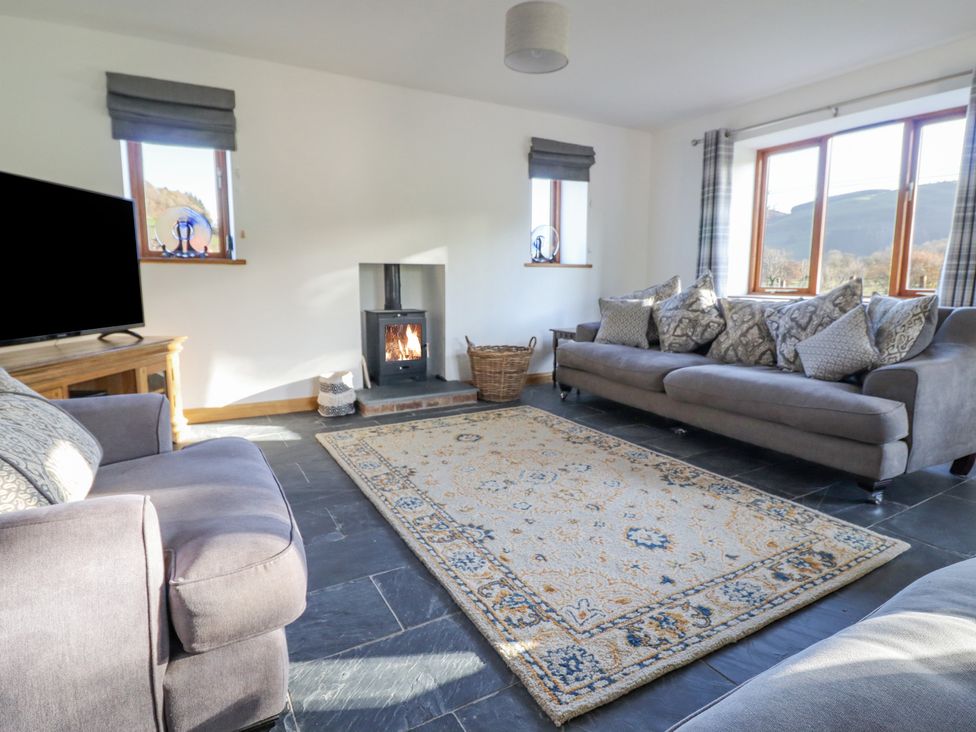 A living room with two gray sofas a patterned rug a wood burning stove and a television at Cwmwr in Penybontfawr