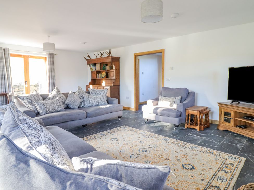 A living room with sofas and cushions a wooden cabinet and a television at Cwmwr in Penybontfawr