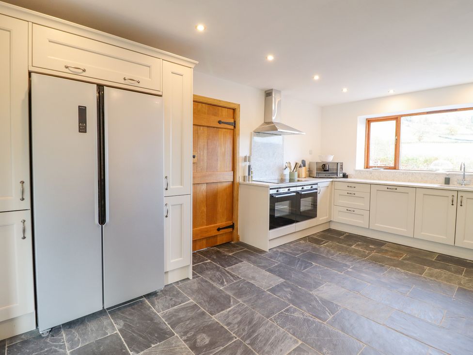 A kitchen with white cabinets a double oven a side-by-side refrigerator a wooden door a microwave and a large window at Cwmwr in Penybontfawr