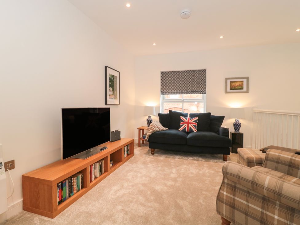 A living room with a black sofa with a British flag cushion a plaid armchair a wooden TV stand with books and a television at Flat 2 in Bournemouth