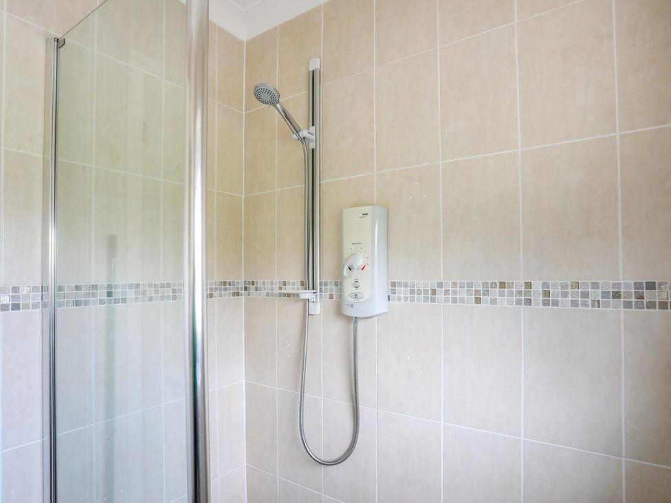 A tiled shower area with a handheld showerhead and glass door at Swn Y Mor in Benllech