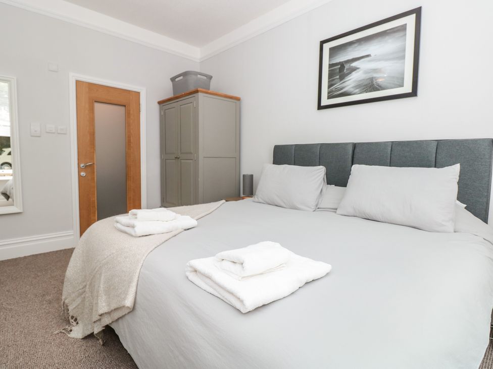 A bedroom with a double bed pillows and folded towels on it a wooden door a wardrobe and a framed picture on the wall at Flat 1 Byfield in Torquay