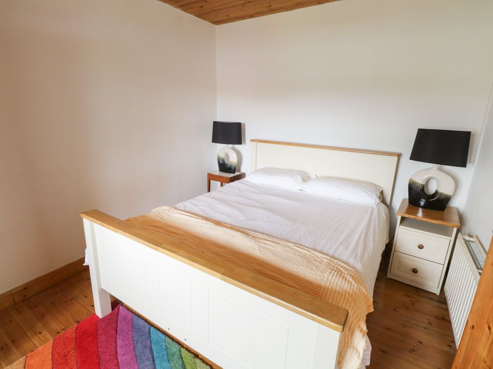 A bedroom with a wooden bed and two bedside tables with lamps and a colorful rug on the wooden floor at Tom's Cottage in Rosmoney near Westport County Mayo