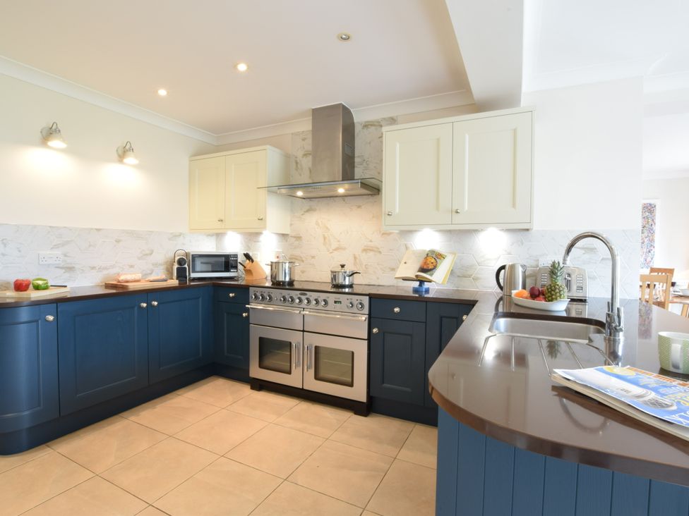 A kitchen with blue lower cabinets cream upper cabinets a stove microwave and a countertop with a sink and fruit bowl at Seadrift Dunwich Near Westleton