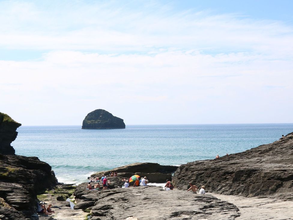 People sitting on rocky shore near the ocean with an island in the distance at Salty Sea Dog in Trebarwith Strand near Tintagel