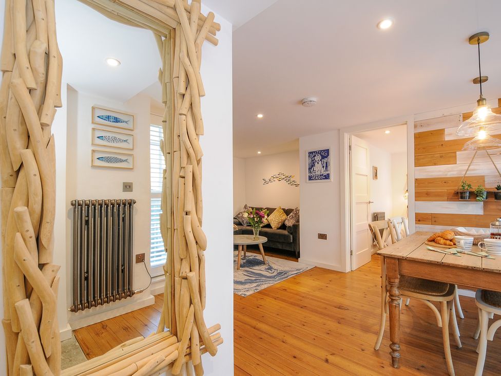 A dining area with wooden table and chairs next to a living room with sofa and decorative pillows at Salty Sea Dog in Trebarwith Strand near Tintagel