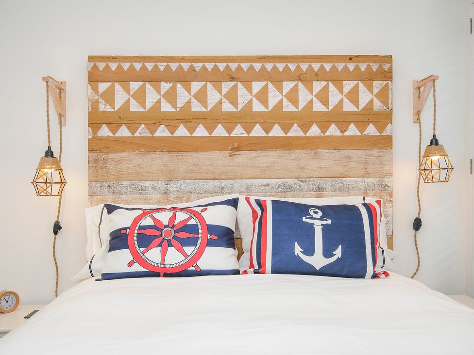A bed with nautical themed pillows and a wooden headboard with wall-mounted hanging lights at Salty Sea Dog in Trebarwith Strand near Tintagel