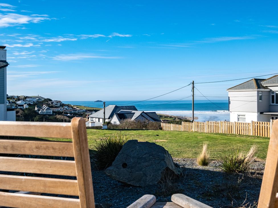 A coastal view with houses a grassy area a wooden fence and chairs overlooking the sea at Blue Ridge in Polzeath