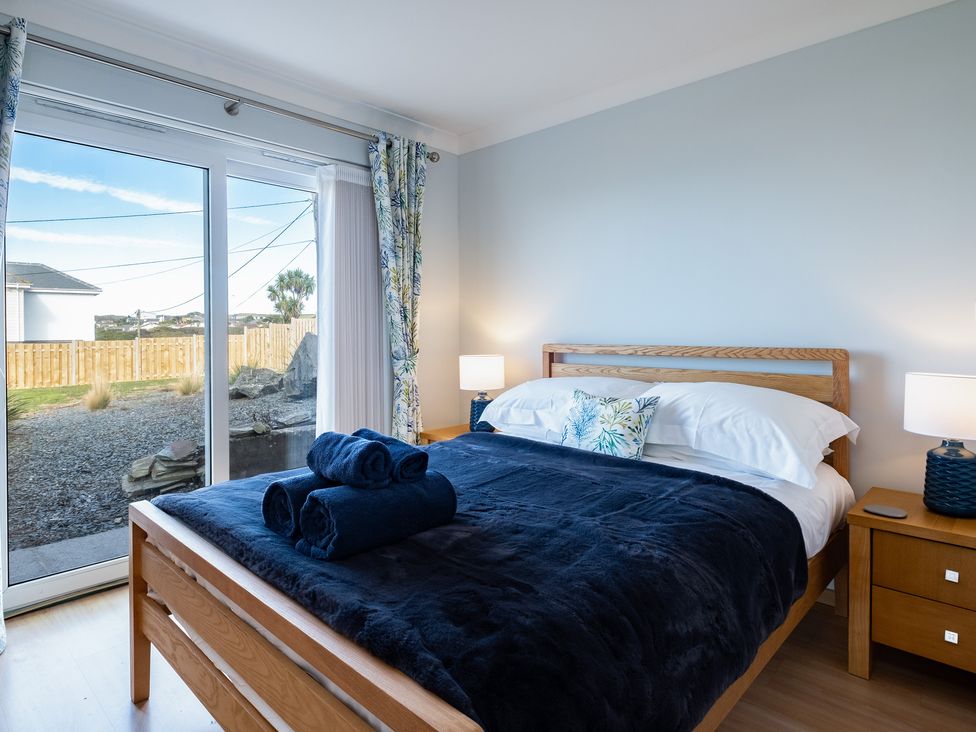 A bedroom with a wooden bed with navy bedding and rolled towels next to sliding glass doors at Blue Ridge in Polzeath