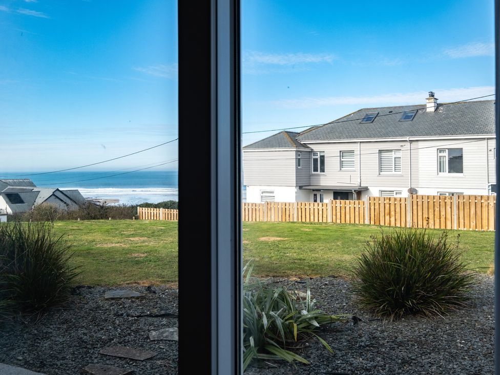 A garden with grass and plants visible through a window with houses and the ocean in the background at Blue Ridge in Polzeath