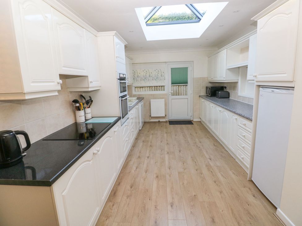 A kitchen with white cabinets appliances and wooden floor at 30 Long Shepherds Drive in Newton near The Mumbles