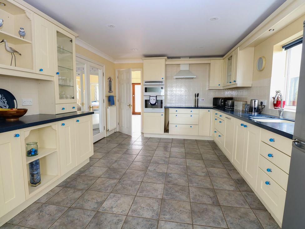 A kitchen with cream cabinets blue handles and tiled floor at Drifters in Winterton-On-Sea
