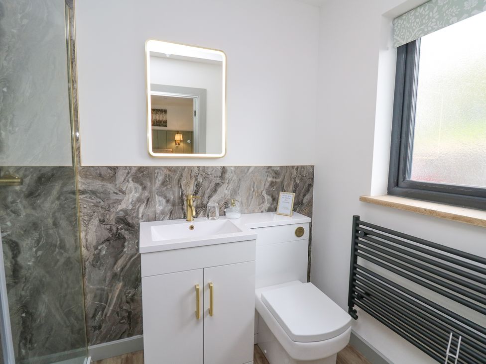 A bathroom with a white sink cabinet and toilet next to a window and a black towel radiator at Barcud Coch - Red Kite in Garthmyl