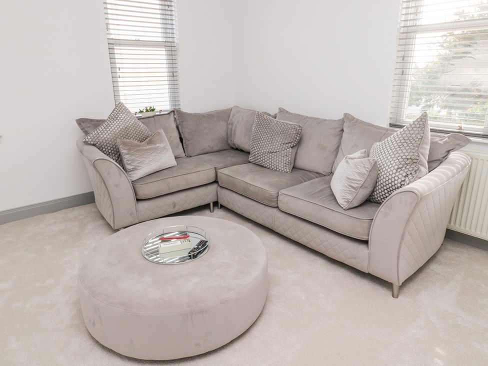 A living room with a grey sectional sofa and a round ottoman with a tray on top at The Annexe in Berwick-Upon-Tweed