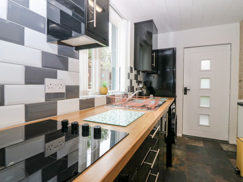 A kitchen with a wooden countertop black cabinets a stovetop a sink a white door and a window at Rosedale in Falkland
