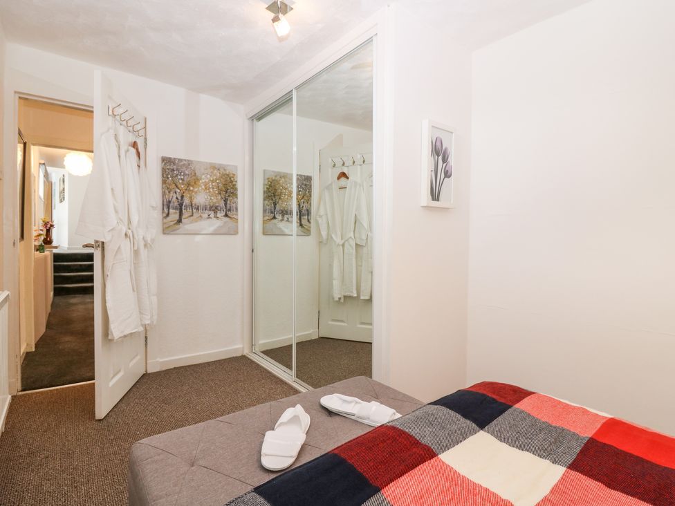 A bedroom with a bed covered in a checkered blanket slippers on the bed a door with white robes hanging a wall with a wardrobe with mirrored sliding doors and paintings at Rosedale in Falkland