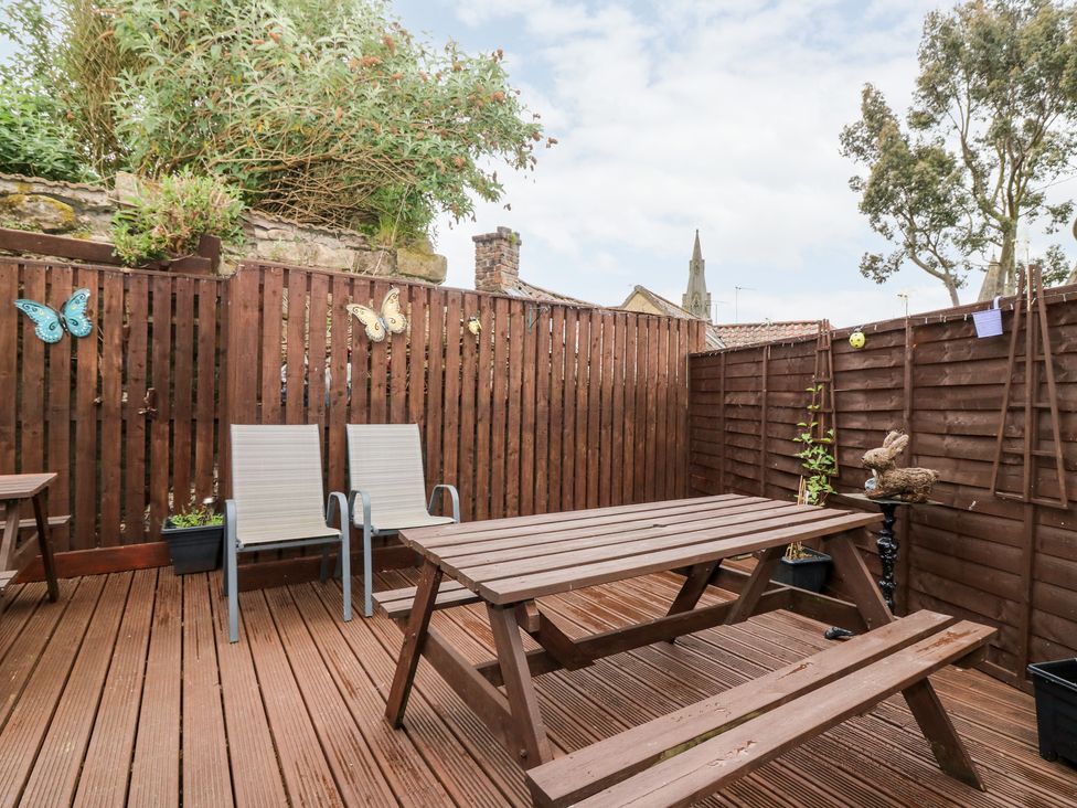 An outdoor patio area with wooden picnic table benches two chairs brown wooden fencing and decorative butterflies Rosedale Falkland