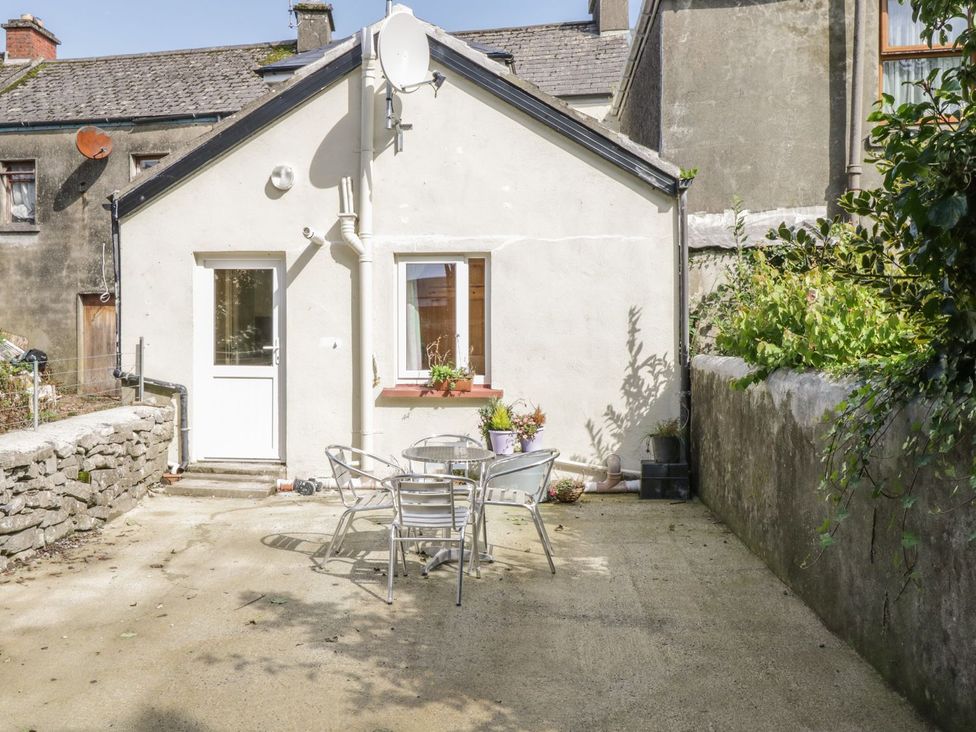 An outdoor patio with a metal table and four chairs in front of a white house wall with a door and window at Glebe House in Ballinrobe County Mayo