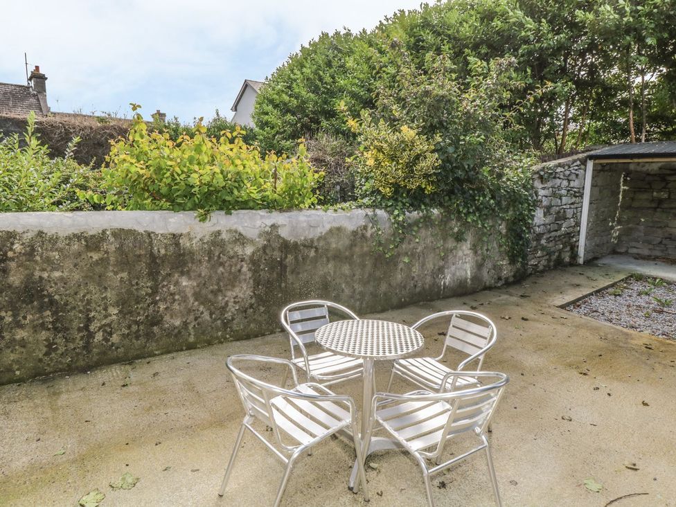 An outdoor patio area with a round metal table and four metal chairs near a stone wall with greenery and a small covered stone structure at Glebe House in Ballinrobe County Mayo
