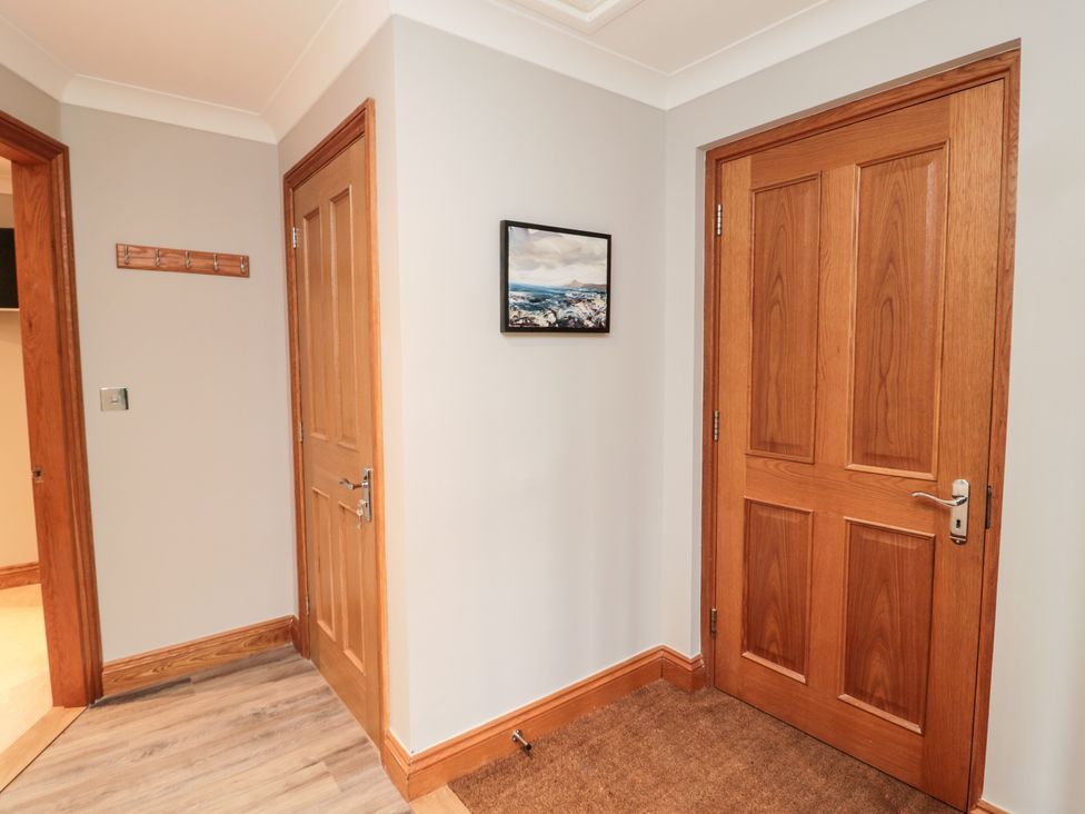 A hallway with three wooden doors a coat rack on the wall a painting and a brown doormat at 2 Apple Tree in Beadnell