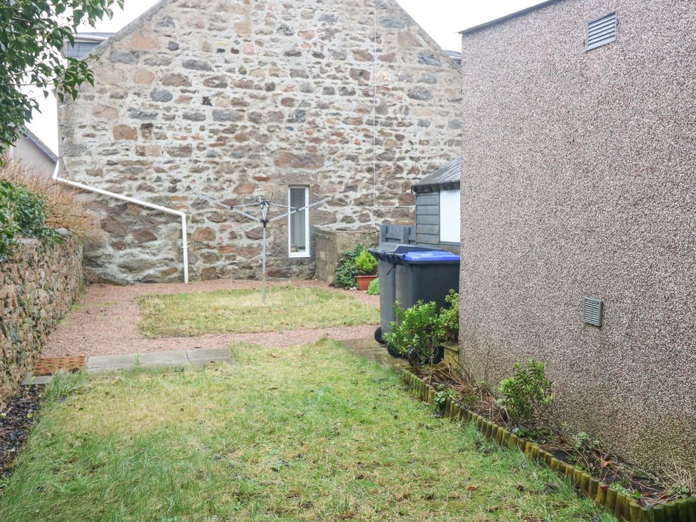 A backyard with grass a rotary clothesline two trash bins and a stone wall at 16 Main Street Newburgh near Ellon