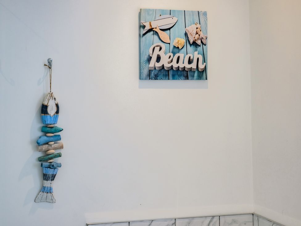 A wall with a hanging wooden fish decoration and a framed beach sign at Harbour Lights Port Isaac