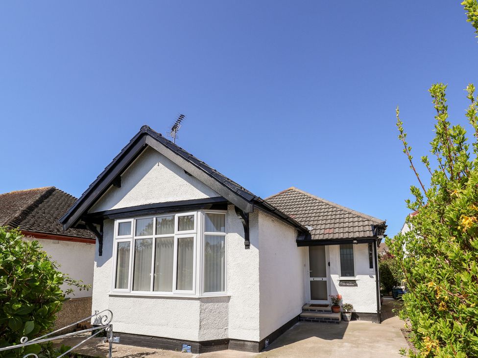 A white single-story house with a tiled roof and a front window with curtains surrounded by plants at 3 Rhyd Drive in Rhos-On-Sea