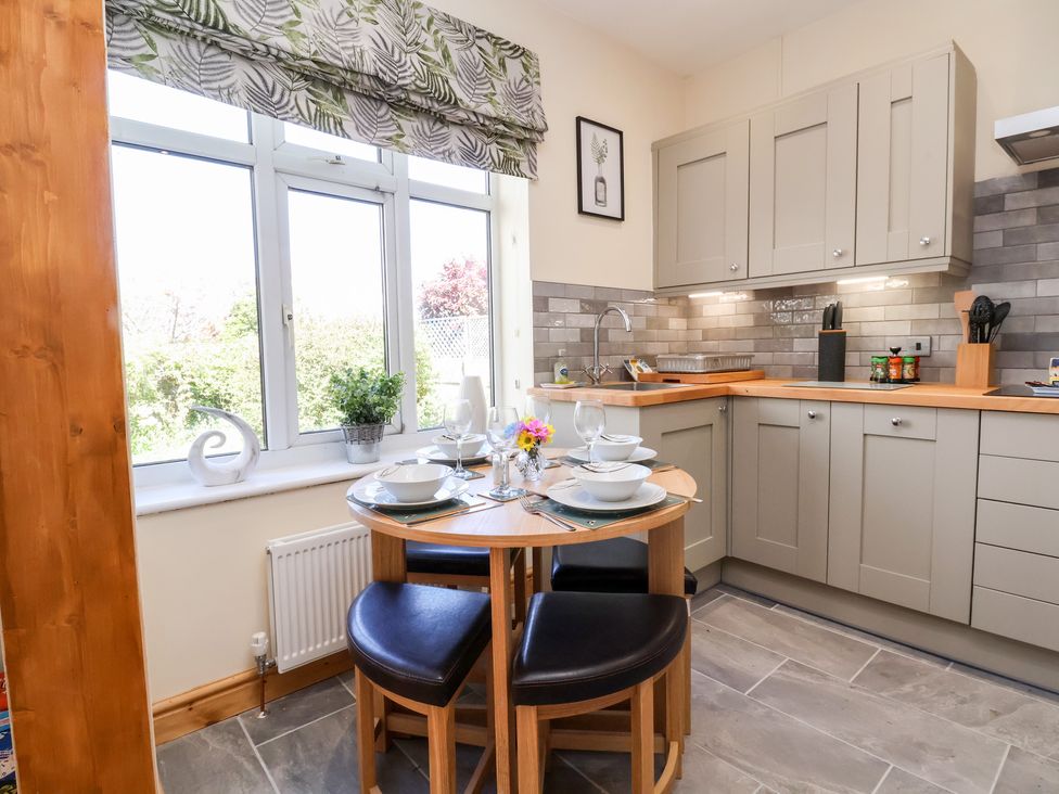 A kitchen with grey cabinets a small round dining table set for four and a window with leaf patterned blinds at 3 Rhyd Drive Rhos On Sea