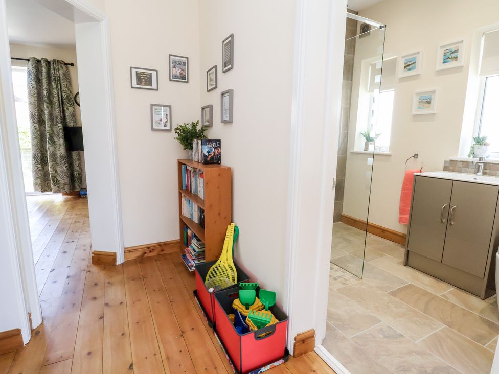 A hallway with a wooden floor a bookshelf toys on the floor and a bathroom with tiled floor visible at 3 Rhyd Drive in Rhos-On-Sea