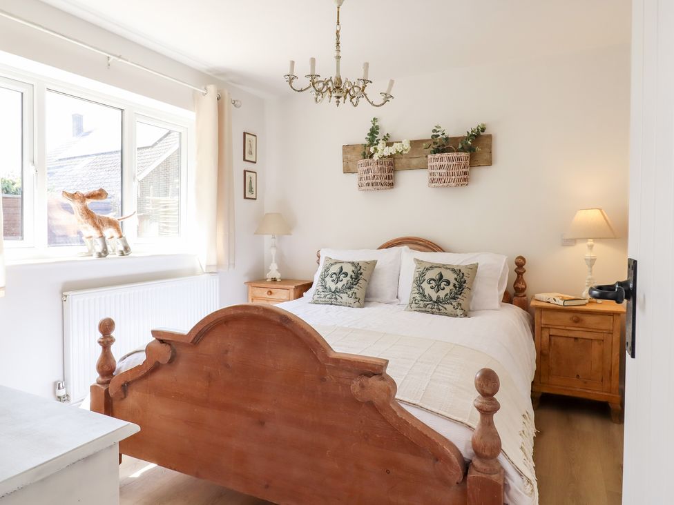 A bedroom with a wooden bed white bedding two bedside tables with lamps and a window with beige curtains at Pantiles in Eyke near Woodbridge