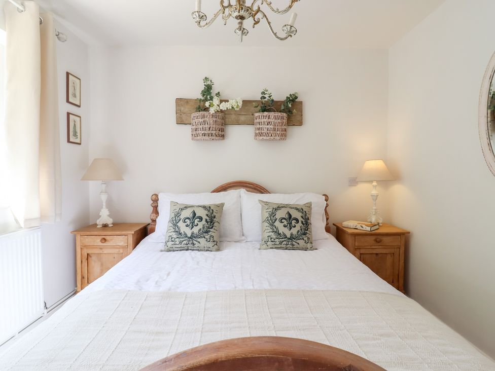 A bedroom with a wooden double bed two bedside tables with lamps and wall decor at Pantiles in Eyke near Woodbridge