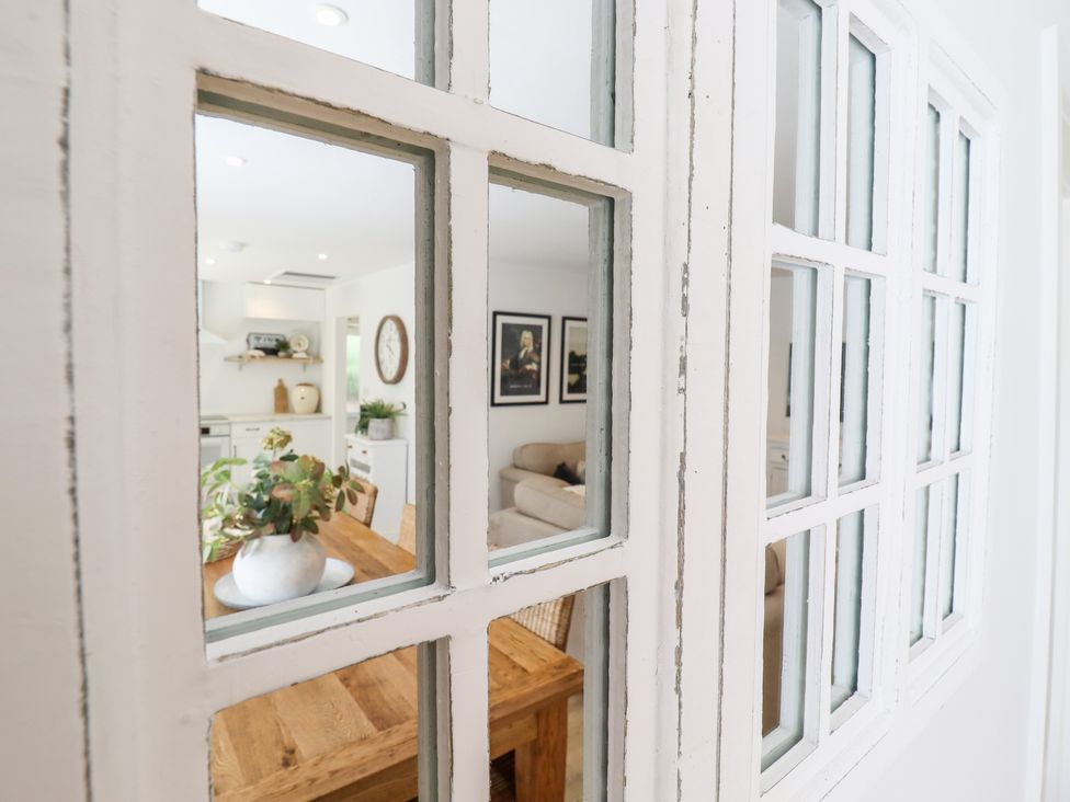 A view through glass panes onto a wooden dining table with a plant vase and a living room with framed pictures at Pantiles in Eyke near Woodbridge