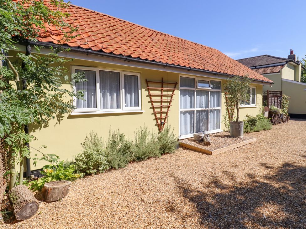 A yellow house with a red tiled roof and white windows surrounded by a gravel yard with plants and wooden planters at Pantiles in Eyke near Woodbridge