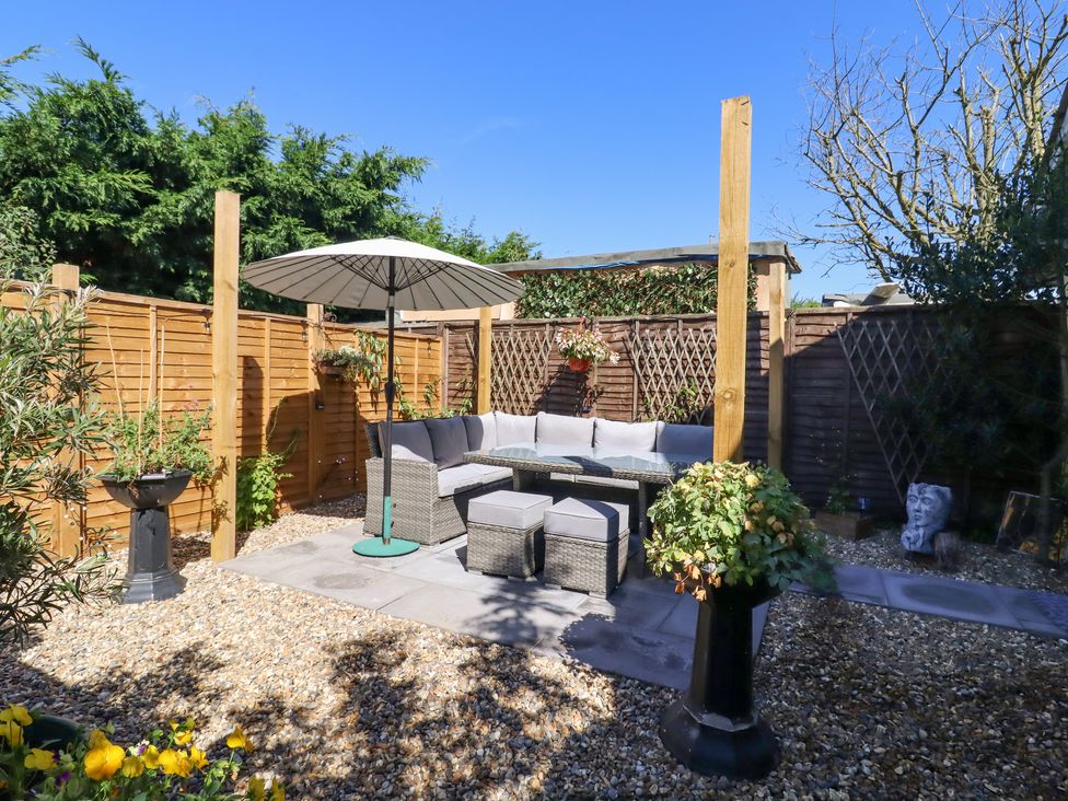 An outdoor patio with a sectional sofa a table and umbrella surrounded by wooden fences and plants at Pantiles Eyke near Woodbridge