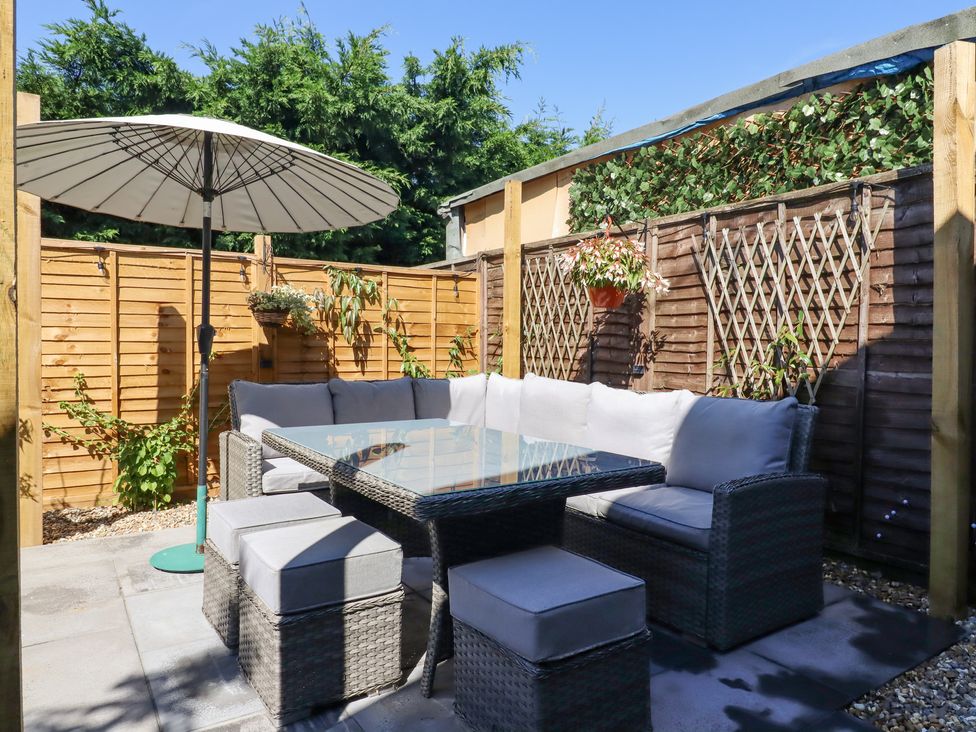 An outdoor seating area with a glass table cushioned chairs ottomans an umbrella and wooden fenced garden at Pantiles in Eyke near Woodbridge