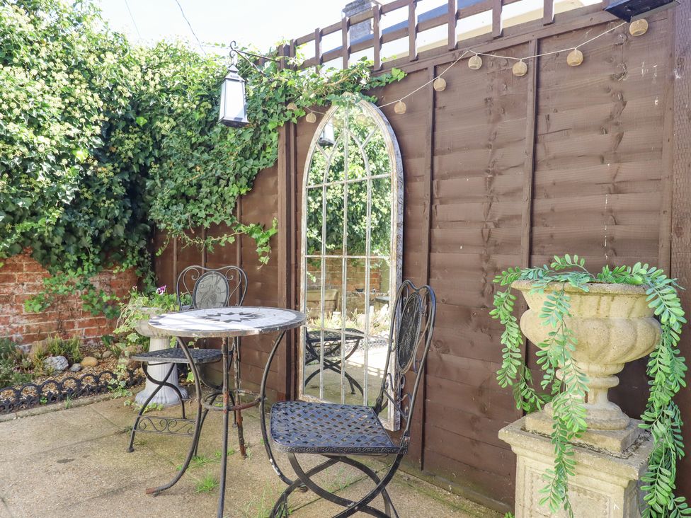 A small outdoor patio with a round metal table and two metal chairs next to a wooden fence with a tall mirror and potted plants at Pantiles in Eyke near Woodbridge