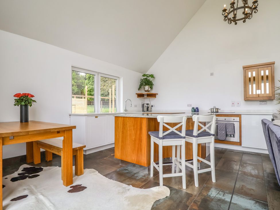 A kitchen and dining area with wooden table and bench a kitchen island with two chairs and a cowhide rug at Polly's Annexe in Levington