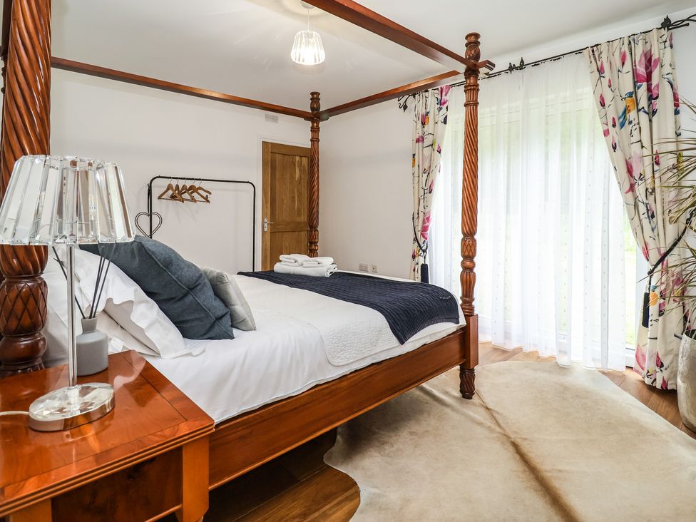 A bedroom with a four-poster bed pillows bedside table lamp floral curtains and a wooden door at Pollys Annexe Levington