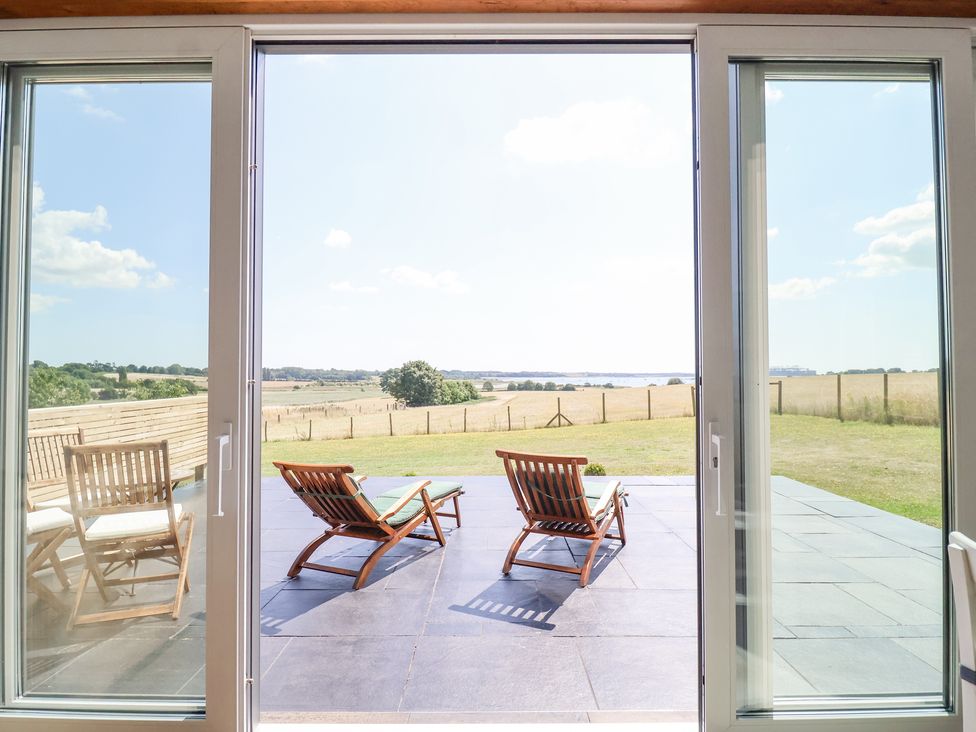 A patio with two wooden lounge chairs and two wooden chairs with a table outside overlooking a field at Polly's Annexe in Levington