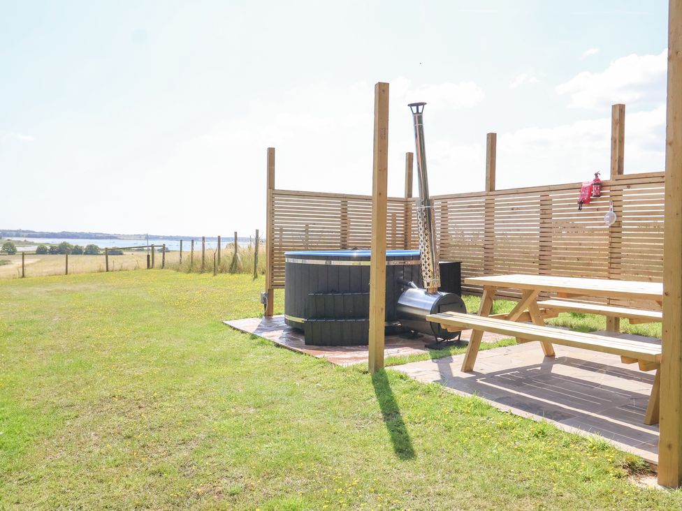 An outdoor area with a wooden picnic table hot tub and privacy screens at Polly's Annexe in Levington