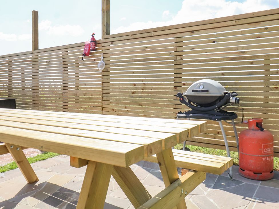 A wooden picnic table and bench with a gas grill and red gas cylinder behind a wooden fence at Polly's Annexe in Levington