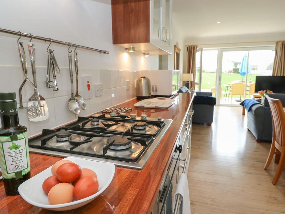 A kitchen counter with a gas stove utensils hanging on the wall and a bowl of eggs overlooking a living area with chairs and a glass door at Cape A1 West Bay Club near Yarmouth