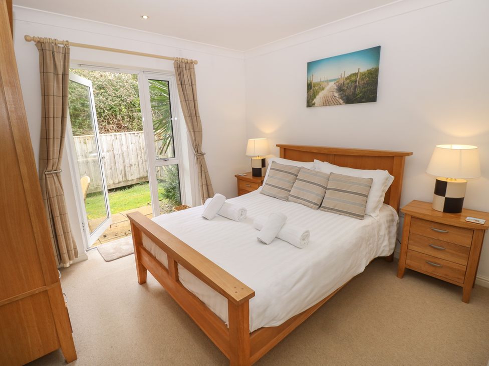 A bedroom with a wooden bed with white bedding and three striped pillows two wooden bedside tables with lamps an open glass door with beige curtains and a picture of a boardwalk on the wall at Cape A1 West Bay Club near Yarmouth