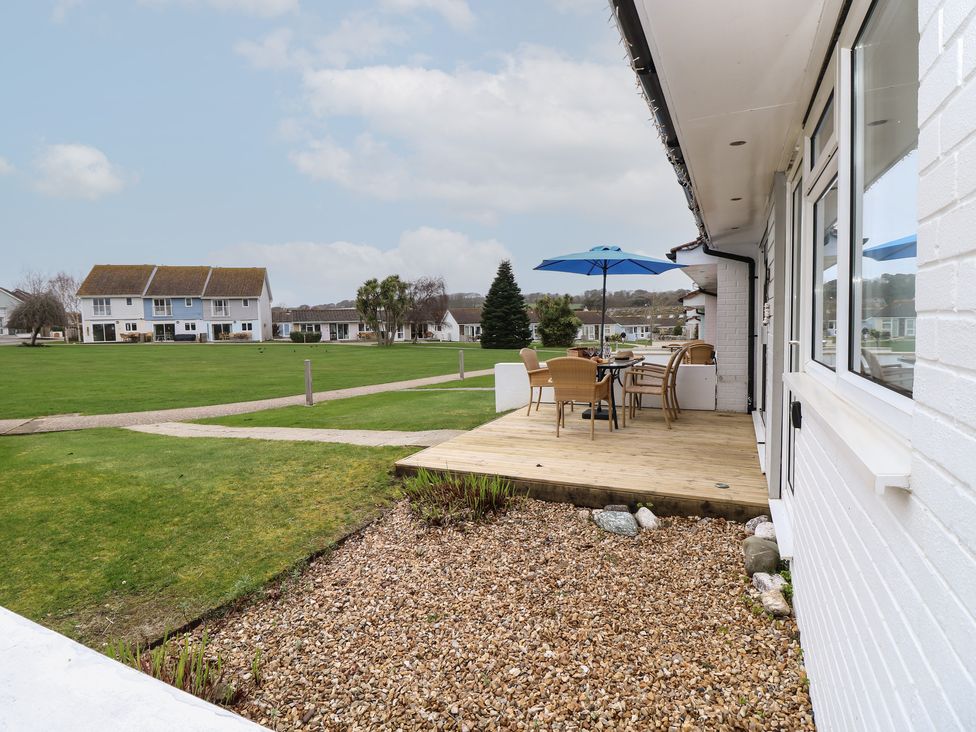 A wooden deck with table chairs and blue umbrella overlooking a grassy area with houses at Cape A1 West Bay Club near Yarmouth