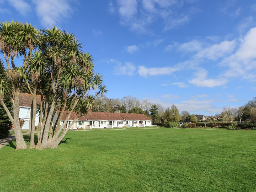 A grassy lawn with palm trees and a row of white houses with brown roofs at Cape A1 West Bay Club near Yarmouth