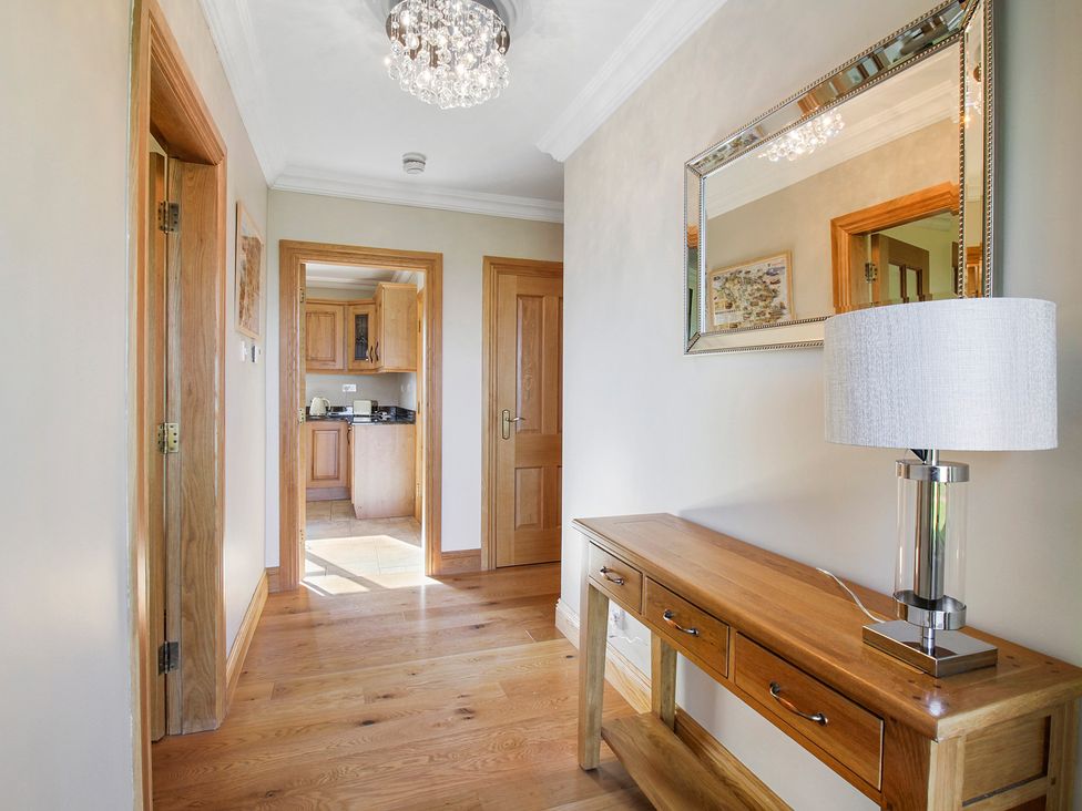 A hallway with wooden floor wooden doors a wooden table with a lamp and a mirror on the wall at Rose Cottage in Muff County Donegal