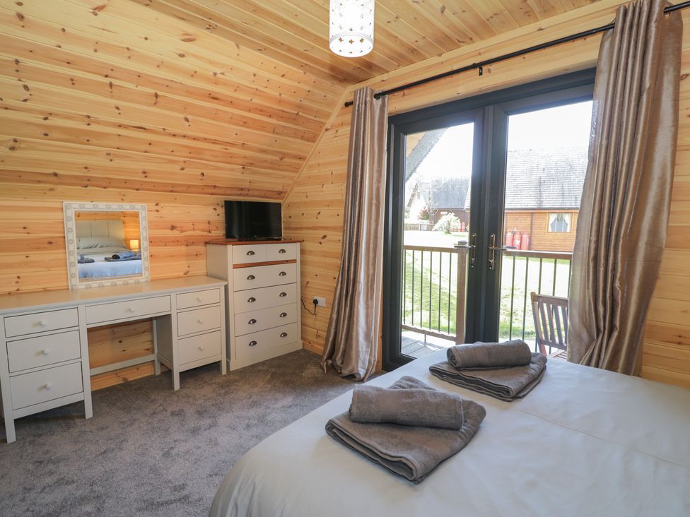 A bedroom with wooden walls a white desk a chest of drawers a bed with folded towels and glass doors leading outside at Sunset Lodge 5 in Llanbedr